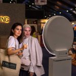 Two guests pose beside a Presto booth at an indoor brand event