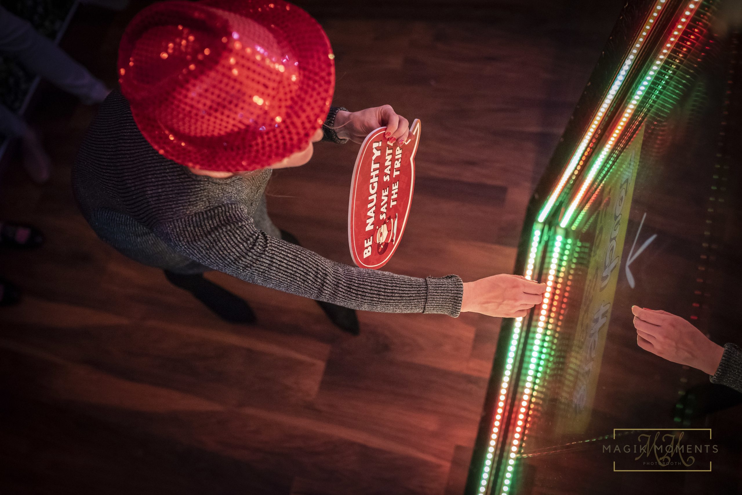 Guest using Magik Mirror photo booth with red sequin hat and holiday sign – Magik Moments Photo Booth